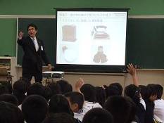 守口小学校の児童が挙手をし、プロジェクターの前でパナソニック株式会社の講師が児童を指名している様子を写した写真