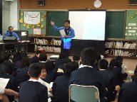 佐太小学校の児童が、プロジェクターの前に立って話をする守口ライオンズクラブの講師の話を聞いている様子を写した写真