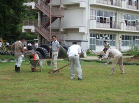 土をまいた芝生化区域の中で道具を使ってならしている作業員たちの姿を写した写真