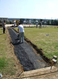 芝生化区画の中央にレンガの小道をつくるため、作業員が小道の部分の土を掘った後に上から砂利を重ねている様子を撮影した写真