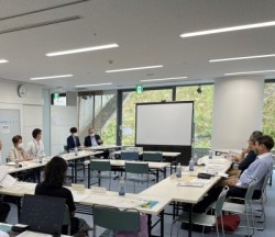2名がモニターの横で説明をし、コの字型に並べられた長机に座った6名がそれを聴いている様子を撮影した写真