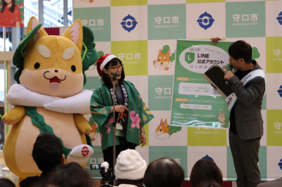 もり吉ふれあいクリスマスパーティーで、司会者の方の紹介でもり吉と楠雄二朗さんが舞台で挨拶をしている写真