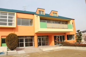 2階建ての建物で、オレンジ色の外壁、緑色の屋根をした児童センターの全景の写真