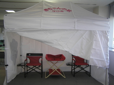 白い布で覆われたテントで、中におむつ替え用のベットと椅子が2脚設置されているテント大の写真