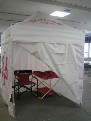 白い布で覆われた屋根付きのテントで中におむつ替えのベットや椅子が準備されているテント小の写真
