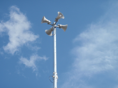 屋外に設置された高いポールの先にスピーカーが4つ付いた防災無線の写真