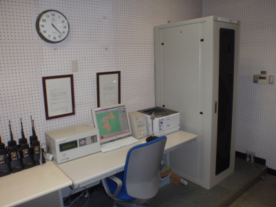部屋の壁沿いにロッカー、机、椅子、パソコン、複数のトランシーバーが横並びに設置されている指令局の写真
