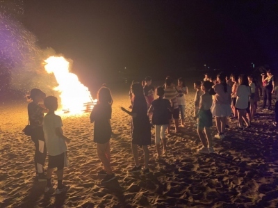暗闇の中、焚き火が灯され、子どもたちがキャンプファイヤーを囲んでいる写真
