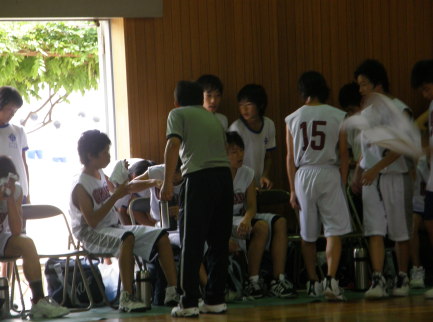 白のユニフォームを着た選手たちがベンチに座ったり、ベンチの近くに集まっている写真