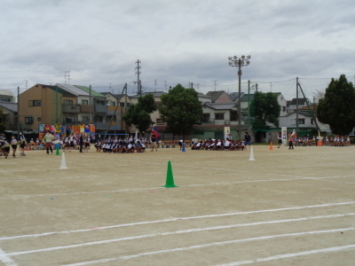 校庭に白や緑の三角コーンが設置されており、組ごとに分かれた生徒たちが競技をしている写真