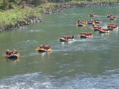 黄色のヘルメットを被った生徒たちがボートに乗って川を進んでいる写真