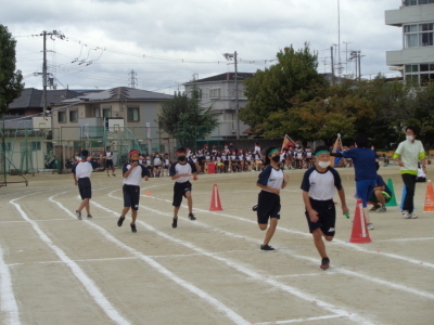 校庭のトラックのライン上でバトンを渡し終えた女子生徒と、バトンを受けて走り出した男子生徒の写真