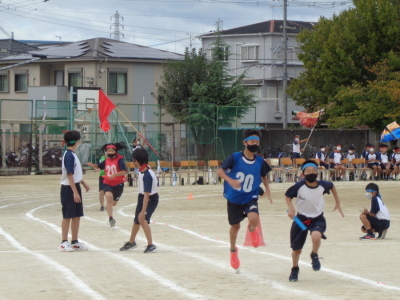 トラックで赤や青のビブスに「20」と書いてある生徒たちが次の走者にバトンを渡している写真