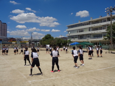 ドッチボールをしている女子生徒たちが並ぶように立っている後ろ姿を写している写真