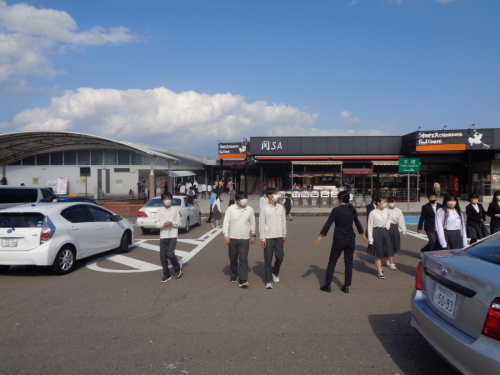 サービスエリアの建物前の駐車場を歩いている学生たちの写真