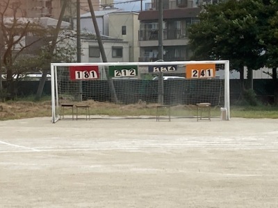 校庭のサッカーゴールの柱に得点が張られており、赤の紙に「161」緑の紙に「212」青の紙に「234」オレンジの紙に「241」と書かれている写真
