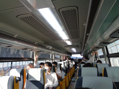 バスの中で、座っている学生がピースをして手を上にあげている写真