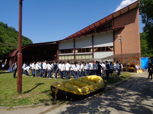 黄色いゴムボートの横に並んでいる学生の写真