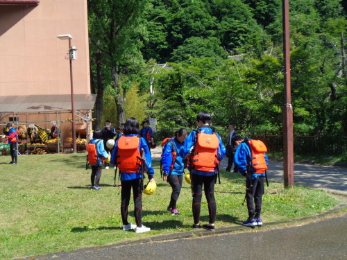 オレンジの救命胴衣をつけ、ウェットスーツに青いジャケットを着た学生の後ろ姿の写真