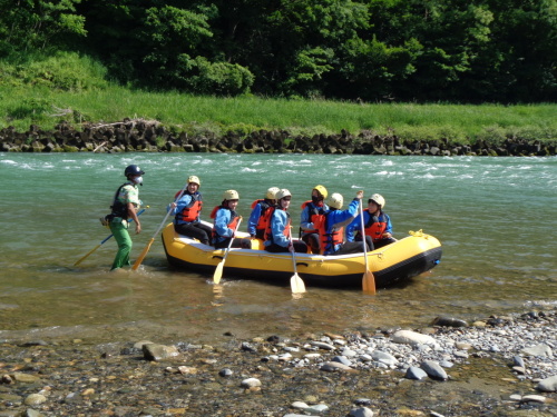 黄色いゴムボートの上に、パドルを持った7名の学生が、着水している写真