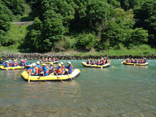 黄色いゴムボートの上の学生たちがバドルを使い進んでいる写真