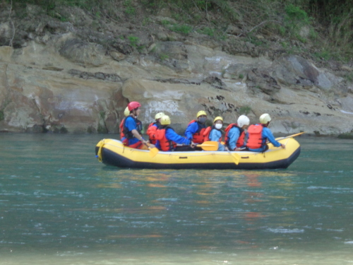 水の中黄色いゴムボートの上でパドルを持った学生たちが座っている写真