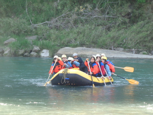 黄色いゴムボートの上の学生たちが、水しぶきを立てながら漕いでいる写真