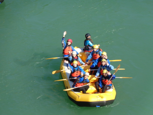 黄色いゴムボートの上の学生たちが大きく手を振ったり、ポーズをとっている写真