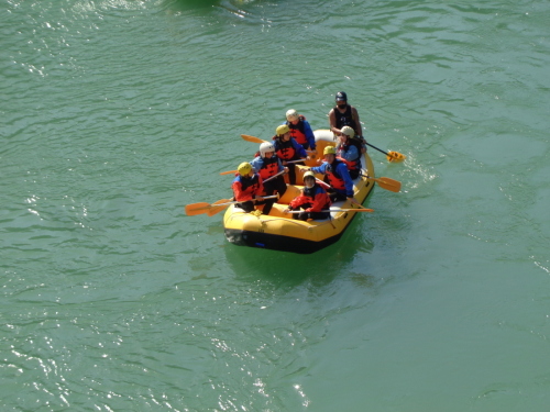 水面が反射する川でラフティングをしている学生を写している写真