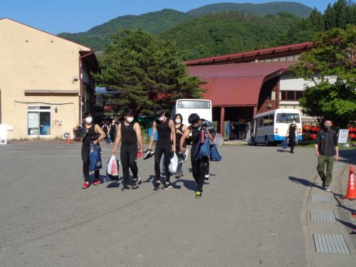 黒いタンクトップに黒いズボンをはいた男子学生が、荷物を持って歩いている写真