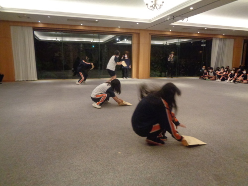 床にある封筒のようなものを勢いよく触っている2名の学生の写真