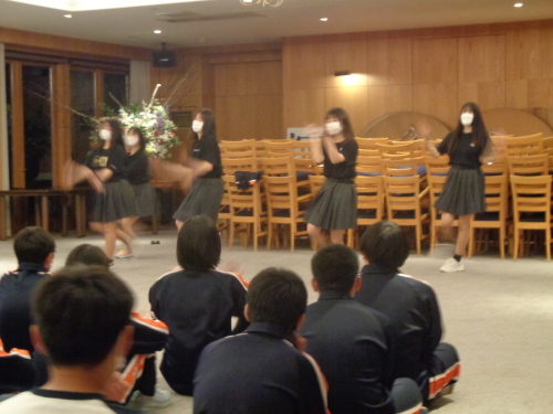 座っている学生達の前で、グレーのスカートに、黒いシャツをきた女子学生5名が踊っている写真