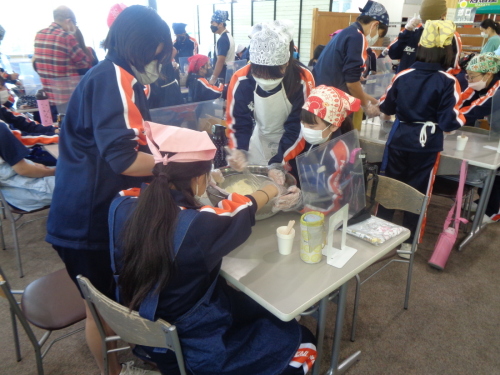 三角巾にマスクをつけた学生が協力して、ボールに入った食材を混ぜている写真