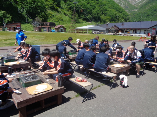 それぞれの机で、串に刺した魚のようなものを焼き台の上で焼いている学生たちの写真