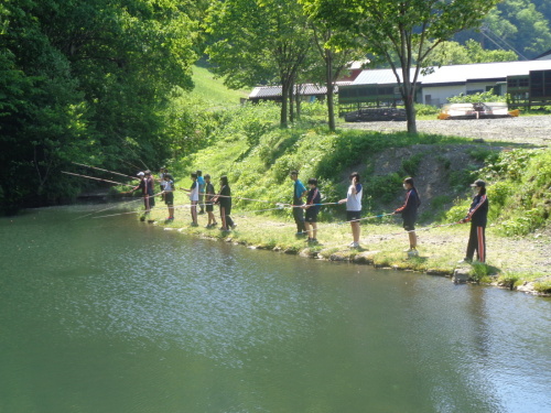 水面が反射する池で、魚釣りをしている学生たちの写真