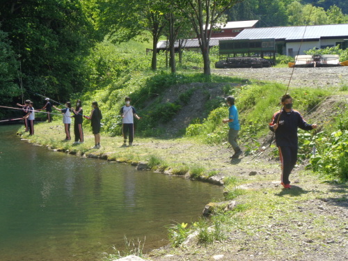 釣り竿を持って、池の周りに立っている学生たちの写真