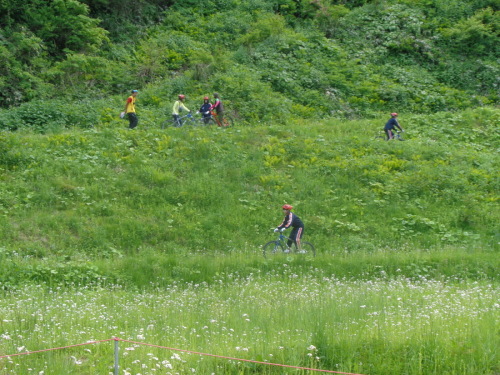 青々とした草が生い茂る草原を、マウンテンバイクに乗った学生が進んでいる写真
