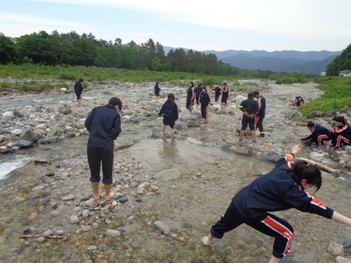 素足の学生たちが浅瀬で、下を向きながら歩いている写真