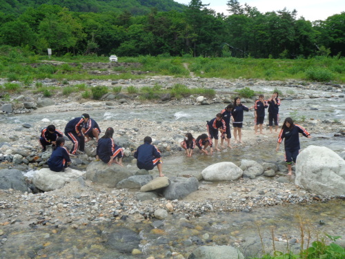 大きな岩の上に座ったり、素足で川に足を付けた学生たちが集まっている写真