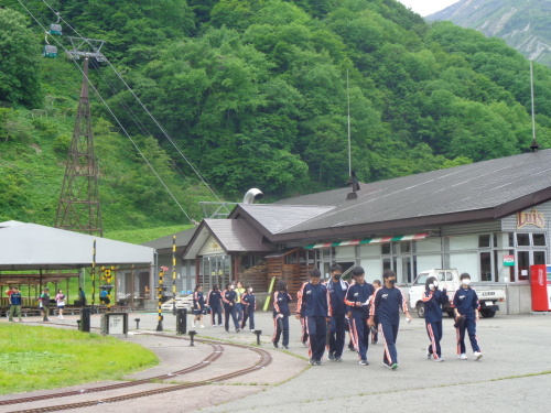 小さな踏切があるレールの横を歩いている学生たちの写真