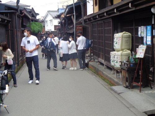 酒樽が飾られた建物の横を、後ろを振り返りながら歩いている学生たちの写真