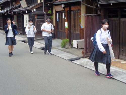荷物などを持った学生が、ピースサインなどをして歩いている写真