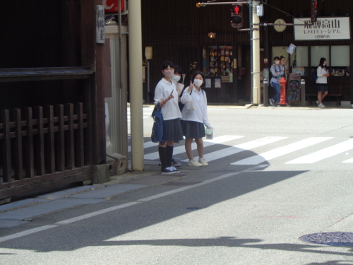 歩道に止まって、ピースサインをしている女子学生3名の写真