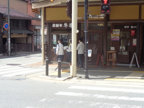 横断歩道の前に並んでいる学生3人を斜め後ろから写している写真