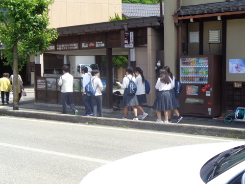 自動販売機の横を歩く学生たちの後ろ姿を少し離れた場所から写した写真