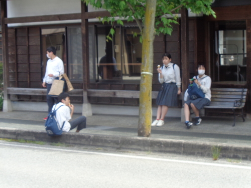 茶色い建物前のベンチ付近で、アイスクリームを食べている学生たちの写真