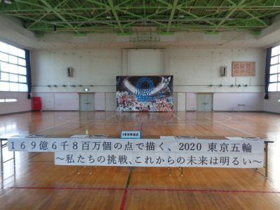 「169憶6千8百万個の点で描く、2020東京五輪～私たちの挑戦、これからの未来は明るい～」と書かれた用紙が貼られ、体育館の奥に大きな絵が展示されている写真