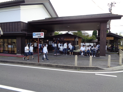 お手洗いの看板が立てられたお土産店前のスペースで生徒たちが休憩する様子の写真