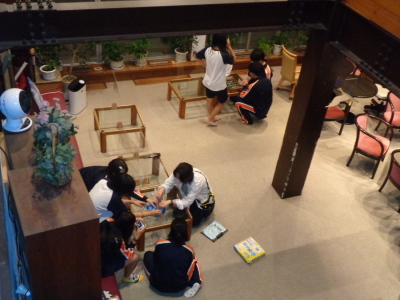 テーブルと椅子が置かれているロビーのような場所で2つのグループの生徒が話合いをしている様子の写真