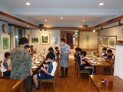 生徒達が夕食が並んでいるテーブルに座り、食事を摂ろうとしている様子の写真